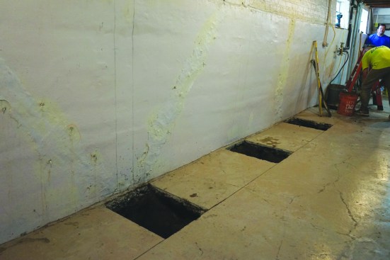 The crew laid out the positions of the vertical beams on the basement walls. After snapping a line across the slab and scoring it with a saw, they removed rectangular sections of the existing slab and dug holes for the beam footings.