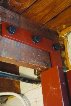 Next, the crew placed each beam in its footing hole on a temporary block that set the beam 6 inches from the bottom of the hole. They rough-plumbed the beam with one flange touching the bulging wall. A flat L-bracket had been welded at the top of each beam with 3/4-inch holes as specified by the engineer. They drilled through the joists and drove high-strength 3/4-inch bolts at each hole location.
