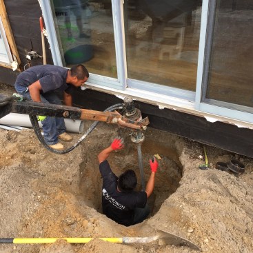 A heavy-duty drill attachment on a skid steer drives the piers into the ground. When one section is driven down near the bottom of the hole, the next section is bolted on and the driving continues.