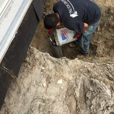After cleaning out the PVC pipe with a high-pressure water hose, a grout mixture is poured into the pipe. A horizontal metal plate is then welded onto the top end of the shaft.
