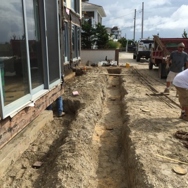 Trenches are excavated for the grade-beam footings. On the left the plates on top of the piers can be seen for the cantilever support. The trench on the right is for the footing that will support the porch. The footing will sit on top of existing PT pilings that have been cut off even with the bottom of the trench.