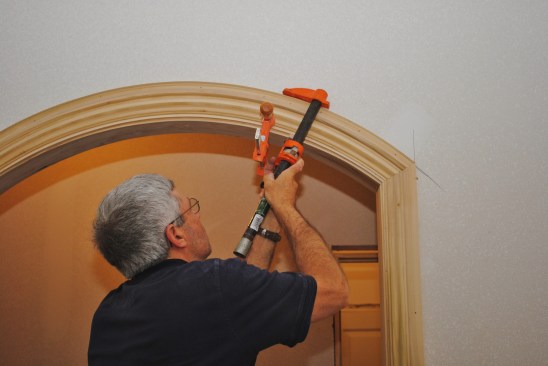 To create an even reveal, a strategically placed clamp draws the jamb into position where it is nailed to the arch to  hold it in place.