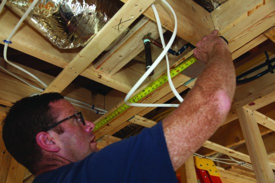 The first step when roughing in a ceiling can is marking out the location. For this shower light, the author first marked the centerline between the back wall and the showerhead.