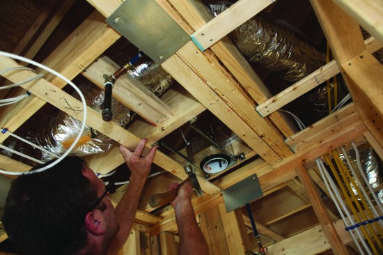 He drives nails to attach the hanger bars to the framing.