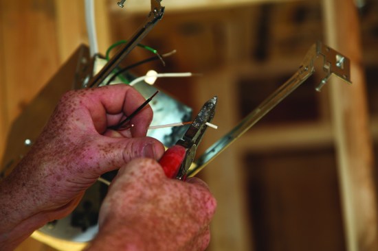 Next, he strips about 1/2 inch of insulation from the white and black conductors of the switch leg.