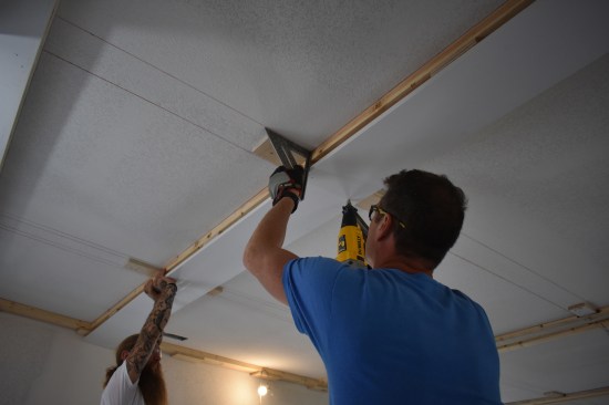 The finished surface for the major beams is primed pine 3/4-inch thick. The crew carefully aligns the finish lumber with the 2-by nailer above before nailing it in place.