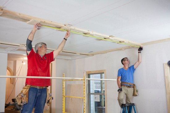 The location of the ceiling cans would not work with the beam grid, so the crew opted to install low-profile LED lighting in the beams instead. Here they measure off the wall to locate the light at the intersection of the beams.