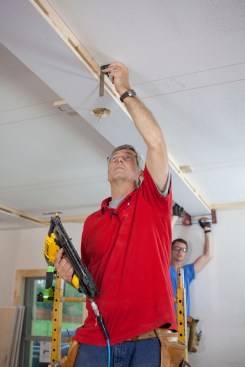 The space between the 2x4 nailers makes a good pathway for the electrical cable for the relocated lights. After leading the cable through the hole drilled for the electrical box,the author aligns the finish layer with the 2-bys above and nails the board in place.