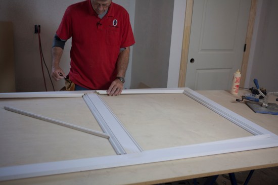 After gluing and stapling 1/4-inch plywood to the back of the panel frame, the author fits panel molding around the inside perimeter of the panel frame.