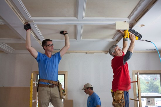 While one crew member holds the panel against the ceiling, another aligns it on the marks and nails it to the ceiling.