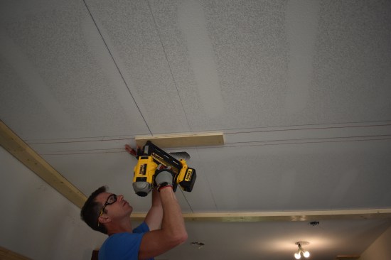 The major beams run parallel to the ceiling joists, so to provide attachment, the crew nails on plywood nailing blocks at the beam intersections. The blocks are long enough to span between two joists.