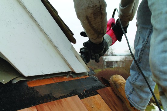 The flashing behind this rake trim needed to be replaced, so a crew member uses a recip saw with a long blade to clip the nails holding the original flashing in place.