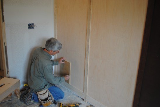 Guided by his reference marks on the floor, the author uses a level and a square scrap of plywood to help locate and mark the electrical boxes on the panels.