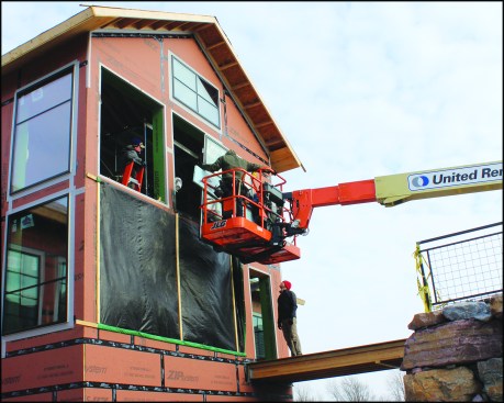 A large triple-glazed fixed window unit manufactured by Fibertec Windows & Doors Mfg. is lifted into place on the building’s south-facing bump-out entry.