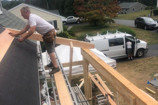 The upper porch was framed with site-built “laminated” 6x6 posts supporting a triple 2x10 girder. The porch roof framing was then tied to the main roof. (The existing shingles were first stripped and ice barrier membrane was installed. Later, the main roof and new porch were shingled with GAF Timberline charcoal laminated shingles.)