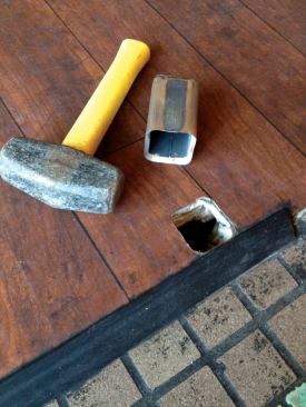 After driving through and removing the top layer of linoleum, I drilled holes just inside my initial cut and continued to drive the square chisel all the way through the floor, alternately driving and drilling as necessary.