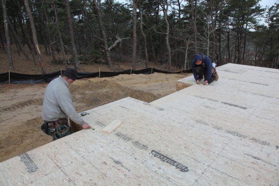 Crew members measure off the perpendicular line they just snapped to lay out the other long walls for that end of the house.