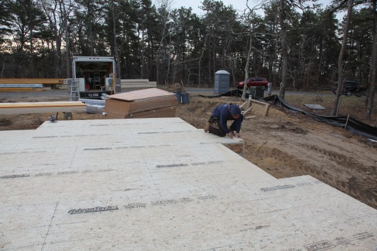 Measuring over the length of the baseline wall and measuring up the length of the opposite wall from the baseline, a crew member marks the last corner for the largest rectangle on the deck. This corner fell in the framing for a bump-out fireplace.