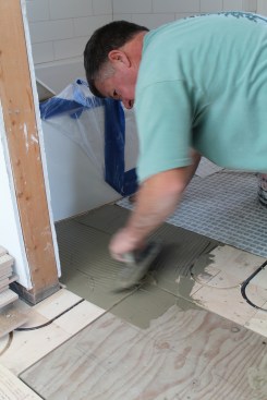 Radiant flooring panels are an excellent choice under a tiled floor. Here, the tile installer applies mortar for the separation membrane that is installed before the tile.