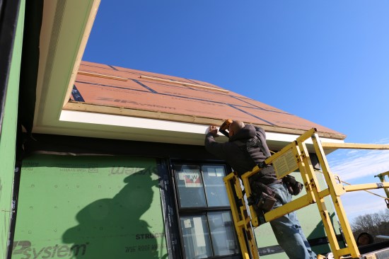 The crew nails the fascia in place. The dado creates a consistent reveal and shadow line along the edge of the cornice.