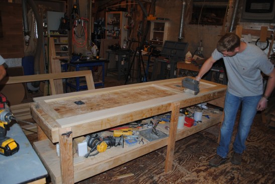 After milling and cutting the parts, the crew assembles the frames using pocket-screws. The frames are joined in pairs to make the doors. Here a layer of glue rolls onto one of the frames before the pairing..