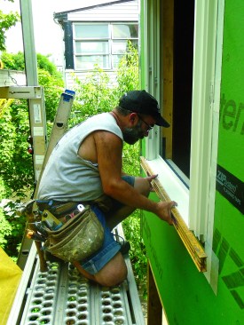 After pressing the window into the wet sealant, the author levels the frame and nails the bottom corners.