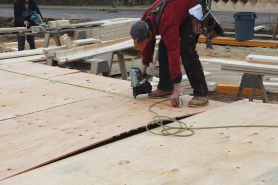 The crew then tacks the sheathing to the studs, using a tape measure to follow the layout.