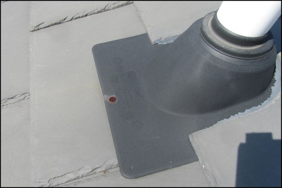 A 15-year plastic boot with a neoprene collar is installed on a “50-year” synthetic slate roof. A heavy-gauge metal flashing sleeve and cap is more appropriate for the life span of the roof.