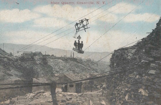 A slate quarry in Granville, NY. circa 1920. As quarry pits got wider and deeper, carriages run on steel cables held aloft by “quarry sticks” were needed to hoist the stone out of the maturing quarries. According to The Slate Roof Bible by Joseph Jenkins, “By 1872, over 11,000 tons of roofing slate were being shipped annually from Poultney, Vermont, amounting to about 35,000 squares of roofing— enough to cover roughly 3,000 average houses.” Image courtesy of the Slate Valley Museum