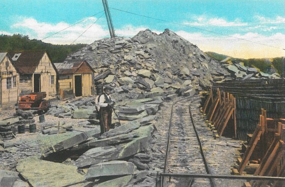A slate quarry in Granville, NY. circa 1920. Shanties line the left side of the yard while stacked slate piles line the right. The completion of the Rutland and Washington Railroad line through Castleton, Poultney, and Granville in 1852 vastly expanded the market for slate beyond the local area to other parts of the northeast and the Midwest. By the turn of the century, up to 250,000 squares of roofing slate were being shipped annually from the slate valley; peaking at 425,000 squares in 1908. Image courtesy of the Slate Valley Museum