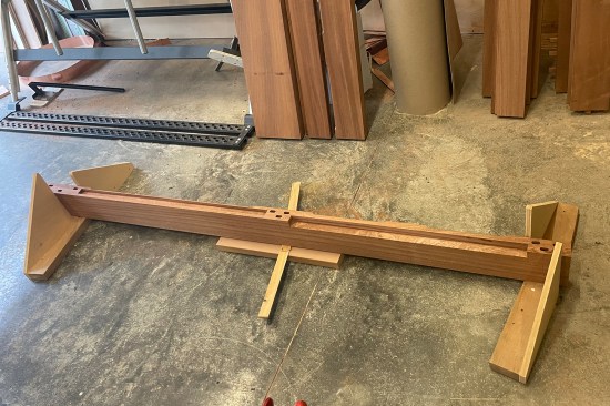 Starting the assembly, a stile is placed into a site-built door stand made out of scrap 2x4 stock and plywood. The middle is shimmed to prevent bouncing when driving the center rail pieces together.