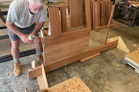 Then, the author sets the first door panel into the routed groove and inserts glue and tenons into the three bottom-rail mortise cuts.