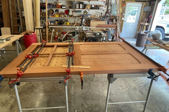 After driving the pieces together on the site-built door stand, the assembly is secured with pipe clamps on both sides on a work table. (Clamping just the top of door leaves the possibility that the joint will open up on the bottom face.)