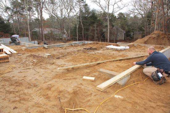 To locate the back corner of the house on the stepped foundation, we again used three sets of hands and a laser. One person held the end of the tape on the back corner of the garage, while a second crew member stretched the tape. Then a third crew member set the laser on a block and moved it until the plumb beam was at the exact measurement for the overall width of the house.