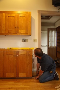 Donbeck sets the cabinet temporarily, checking front and back for level and looking for bows in the floor.