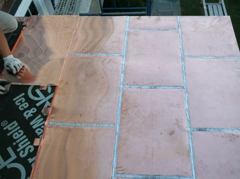 On succeeding rows, we offset the seams in a staggered pattern, like a running bond. The uphill pans overlap the edges of lower pans during installation. The slight pitch of the hip roof did not affect the layout; the copper pans were flexible enough to be bent down without having to alter the layout or the panels themselves.