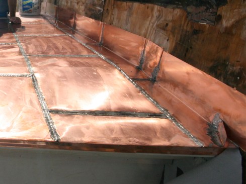 We interlocked the bottom and side seams of the roof-to-wall pans and then fastened the vertical leg with a couple of nails at the very top of the flashing before we soldered the seams. Solder was run up the vertical leg 4 inches or so and a kickout flashing was soldered in place.