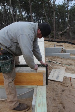 The first line to establish is the baseline, which is usually the longest wall of the house. Using a gauge block made from 2-by plate stock, square off the rim joist of the floor deck and mark the first corner of the baseline wall.