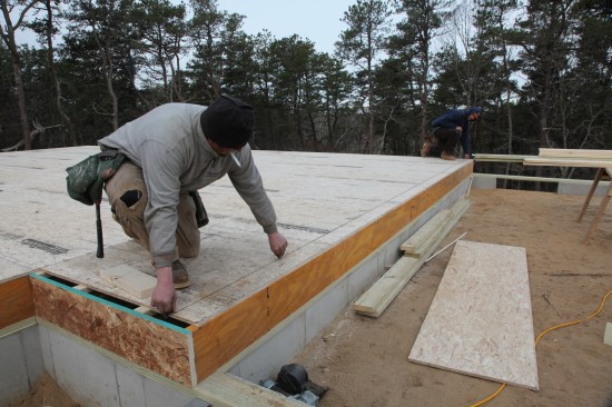 Snap a line from the baseline corner to the adjusted corner. That line for the square wall should be perfectly square to the baseline wall. Repeat the process for the square wall on the other side of the house. Note, the crew in the photos began the wall layout while another crew member was cutting the filler piece of sheathing for the end of the parallel wall. The missing sheathing did not affect the plate layout because the plate line for that wall fell on the installed sheathing.