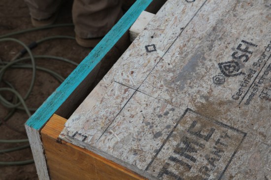 In this close-up of the intersection between the square wall and the parallel wall, the approximate corner is marked in pencil, and the adjusted corner of the intersection is snapped in permanent black chalk lines. (Note:  The edge of the floor sheathing is missing from this photo. The crew will come back and piece this in before standing the 2x6 walls.)