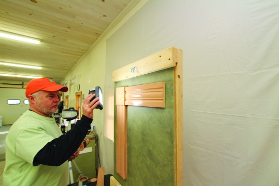 As he brushes on the paint, he uses a hand-held LED light to look carefully at the sheen of the paint to gauge whether the coat is even. Brush strokes should always run in the same direction as the grain of the trim.