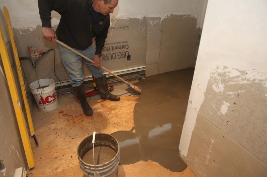The author uses a broom to smooth the edge of the leveler up to the high corner of the room. Note that the leveler is seeping around the corner of the shower.