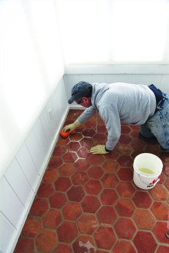After letting the grout cure for a few days, the author cleans the remaining grout haze from the rough surface of the terra-cotta with a muriatic acid wash, which he uses only in extreme cases such as this. To protect his skin and eyes, the author wears heavy-duty gloves and safety glasses. After dampening the tile with clean water, he wipes a 10:1 water-to-acid solution over the tile, causing the grout areas to foam white as the acid cleans the residue from the tile.