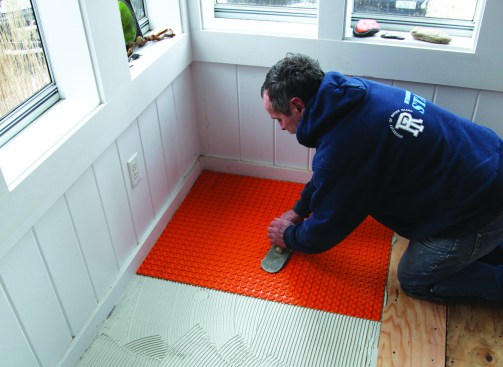 To embed the sheets of uncoupling membrane in the thinset, he applies pressure with a wooden float.