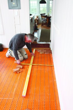 Before installing the tile, he measures from the wall to keep his installation guide—a long level—parallel with the wall.