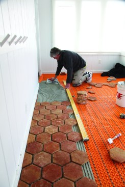 After spreading unmodified thinset with a 3/8-inch notched trowel, a crew member installs the tile using the level as a straightedge against the outermost course.