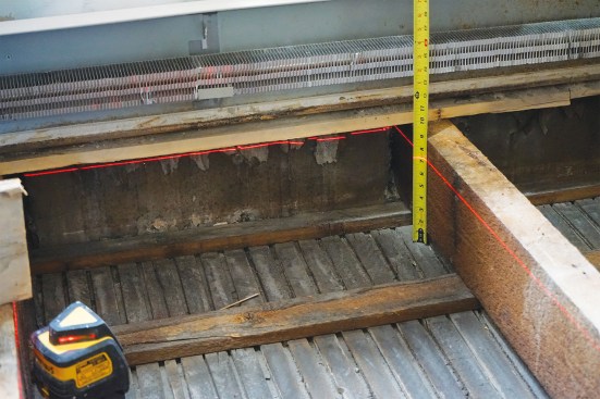 After removing the existing flooring, a level laser line shows 2 inches of wood to be removed at the high end of the 3x8 hemlock joists (above).