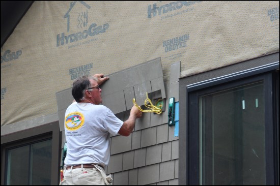 Here, the shingle panel is dry-fit around the fixture block. A circular saw fitted with a fiber-cement saw blade is used to make cut-outs, while a carpenters knife is used to remove material from inside corners as needed. Cut edges are painted with touch-up paint supplied by the manufacturer.