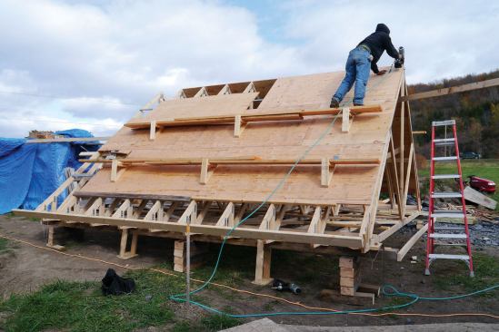 I laid the sheathing out from the peak down, which left a 20-inch opening at the bottom of the smaller roof, giving us a grab hole to move the airborne roof into place, as well as allowing room for fastening the trusses to the top plate. Starting 20 inches up from the sub-fascia, we nailed on the first course of 5/8-inch plywood sheathing. When we got to the top, we reversed course and shingled from the top down.