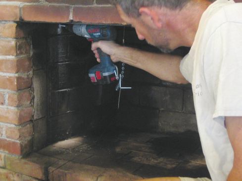 Locate the bracket holes squarely over a firebrick, not on a mortar joint. Mark and drill holes for the expansion fasteners or concrete screws, which are usually supplied in the kit. 

